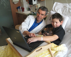 Kind im Krankenbett mit Heilstättenlehrkraft gemeinsam am Laptop